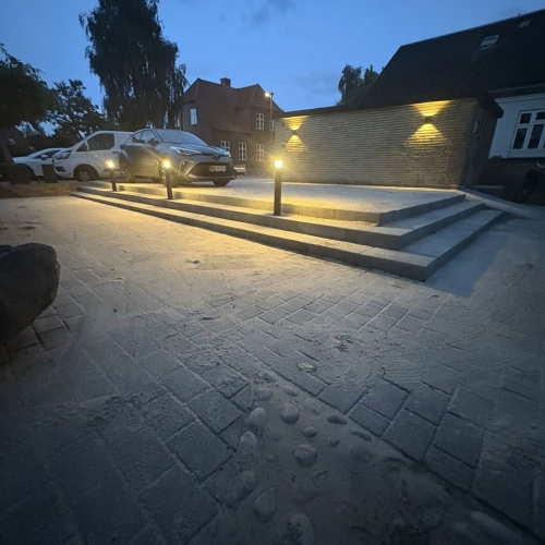 Elegant brolægning foran trappe og parkering med lys, udført af brolægger i Bramming.