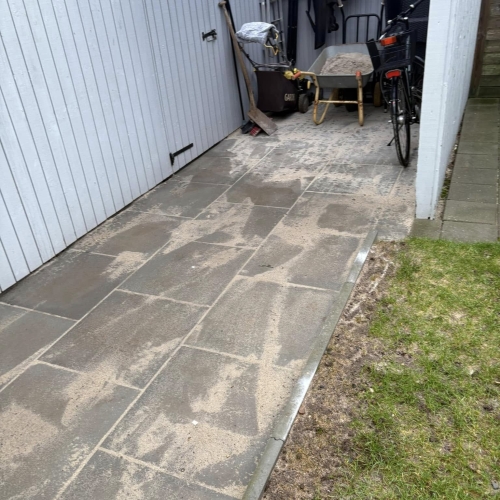 Flisearbejde langs skur og cykel, nybelagt gangsti i Grindsted med sandrester.