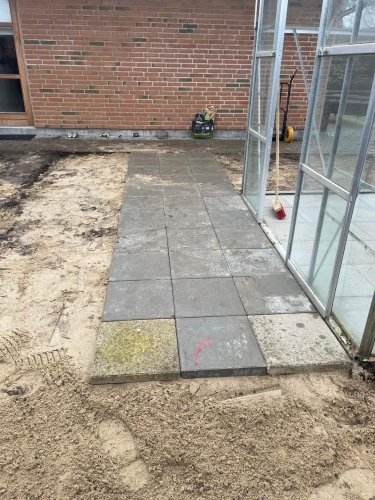 Flisearbejde foran drivhus i Esbjerg med grå betonfliser lagt i række.