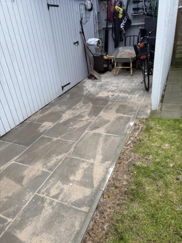 Flisearbejde langs skur og cykel, nybelagt gangsti i Grindsted med sandrester.