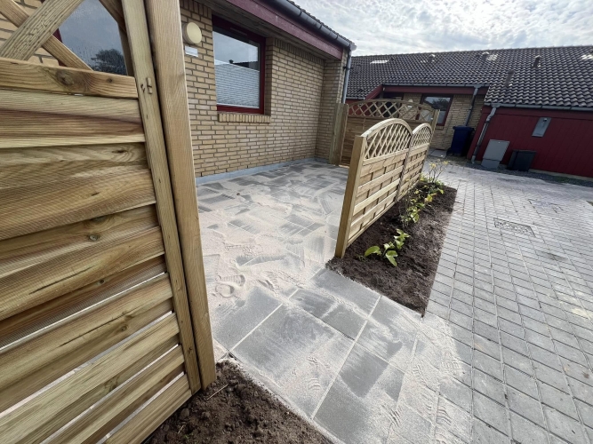 Flisearbejde i Esbjerg – ny fliseterrasse ved rækkehus med træhegn og plantebed.