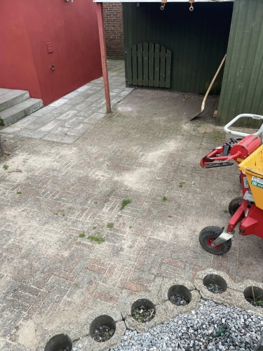 Gammelt fliseområde ved skur i Gørding før renovering – flisearbejde påbegyndt.