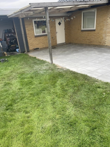 Ny fliseterrasse under overdækning ved bagdør til murstenshus.