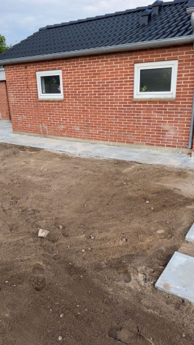 Flisearbejde med ny flisegang langs husets side ved rødt murstenshus i Tjæreborg.